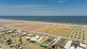 A beach with rows of umbrellas and sun loungers, a playground, and a bar. - Hotel Ravello Rimini (Rimini)