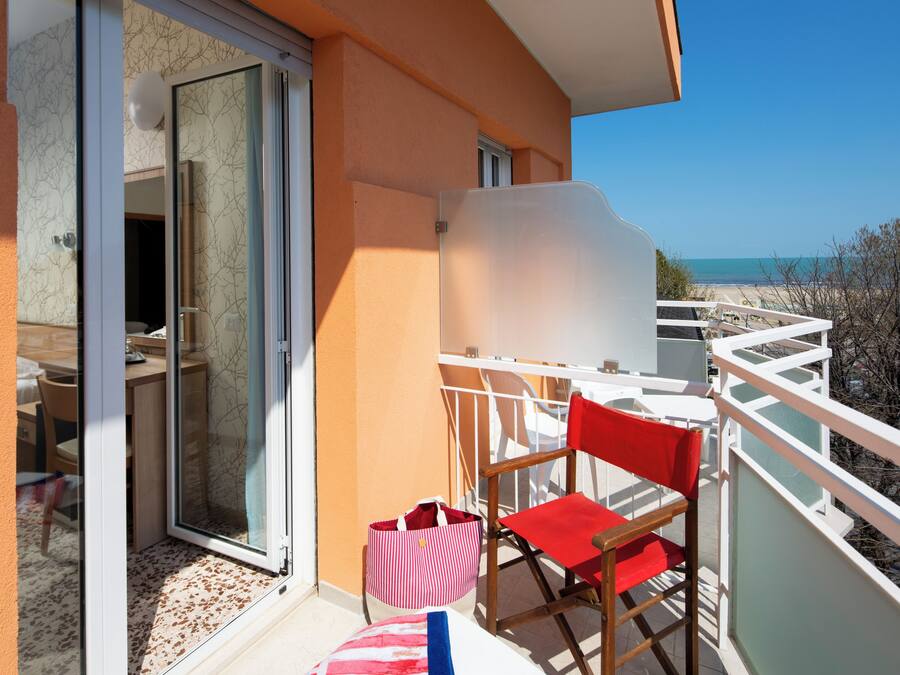 A balcony with a red chair, a striped bag, and a view of the beach.
