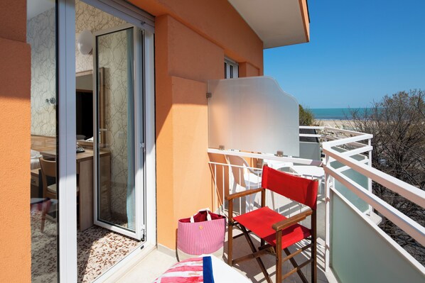 A balcony with a red chair, a striped bag, and a view of the beach.