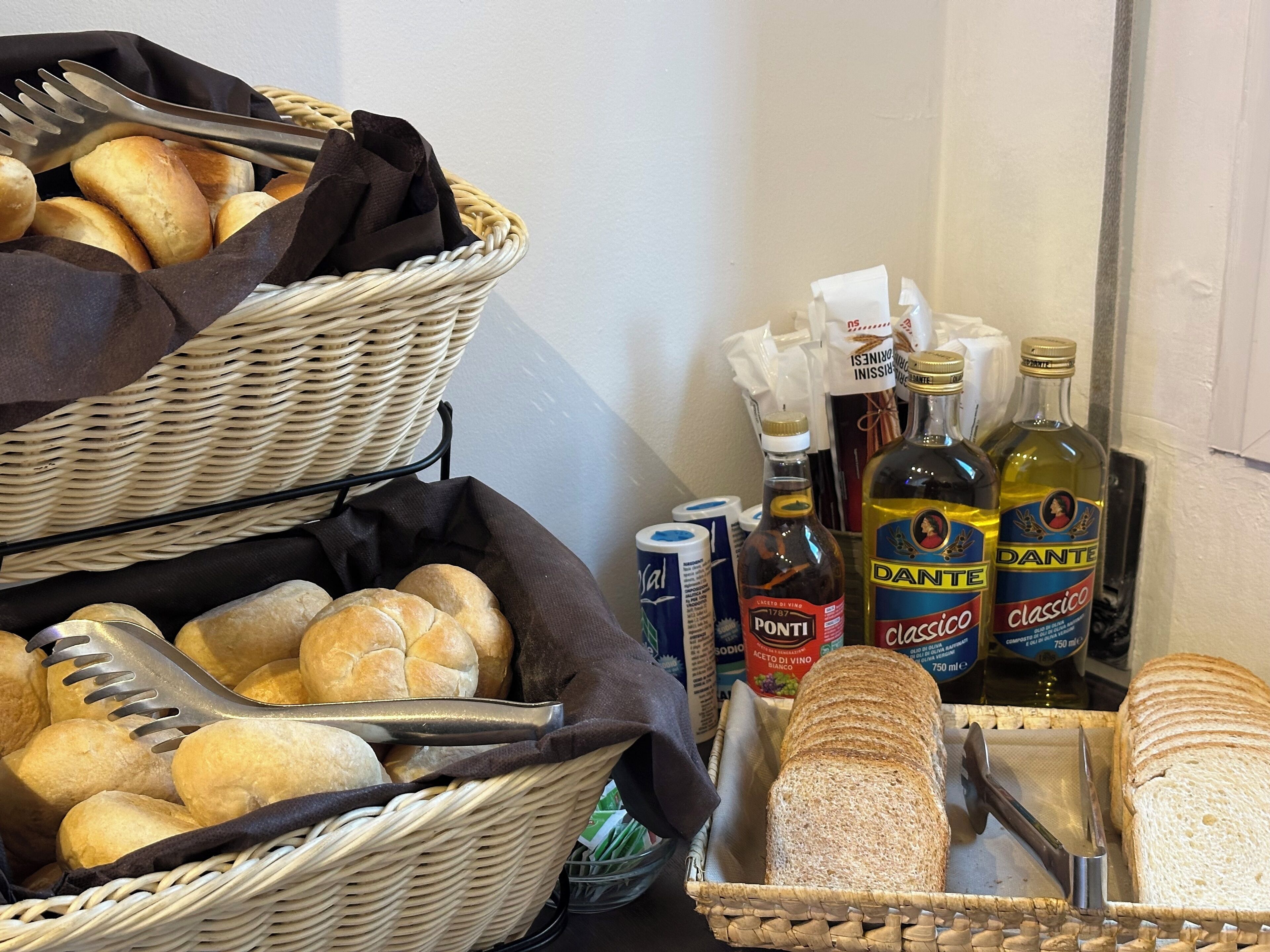 A buffet setup with baskets of bread, bottles of wine, and condiments.