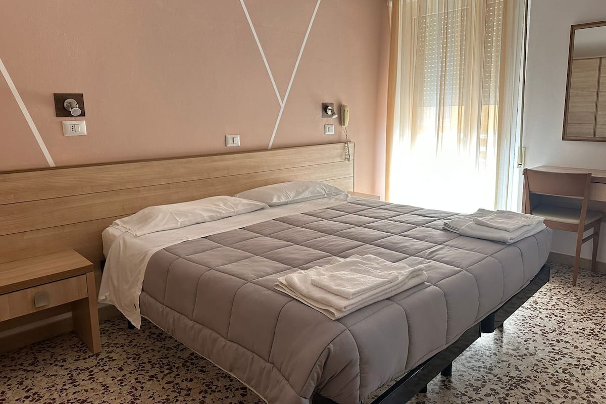 A hotel room with a bed, bedside table, and a desk with a chair.