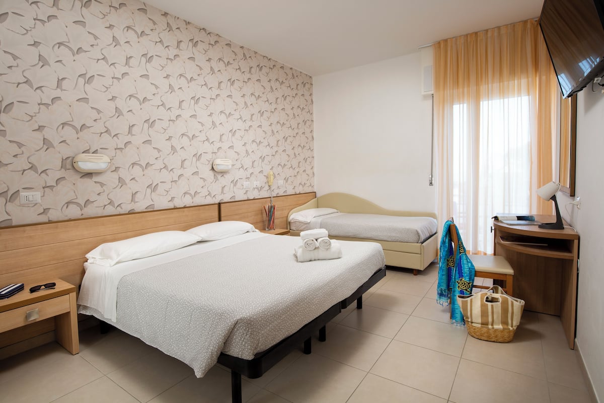 A hotel room with two beds, a desk, a TV, and a window with curtains.