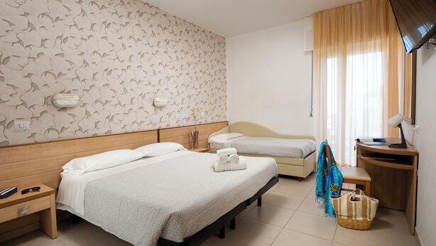 A hotel room with two beds, a desk, a TV, and a window with curtains. - Hotel Ravello Rimini (Rimini)