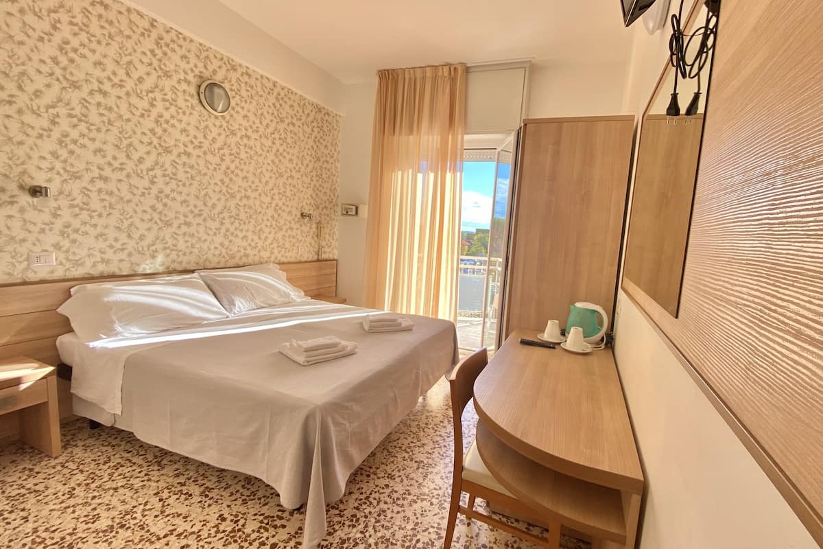 A hotel room with a bed, a desk, and a view of the outside.