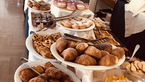 Una mesa de bufé con diversas pastas y postres, incluyendo croissants, muffins y un bol de ensalada de frutas.