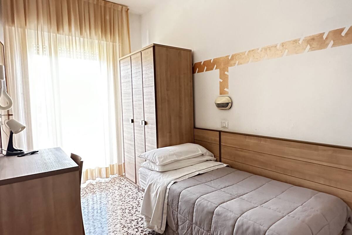 A bedroom with a bed, a wardrobe, a desk with a lamp, and a wall-mounted light fixture.