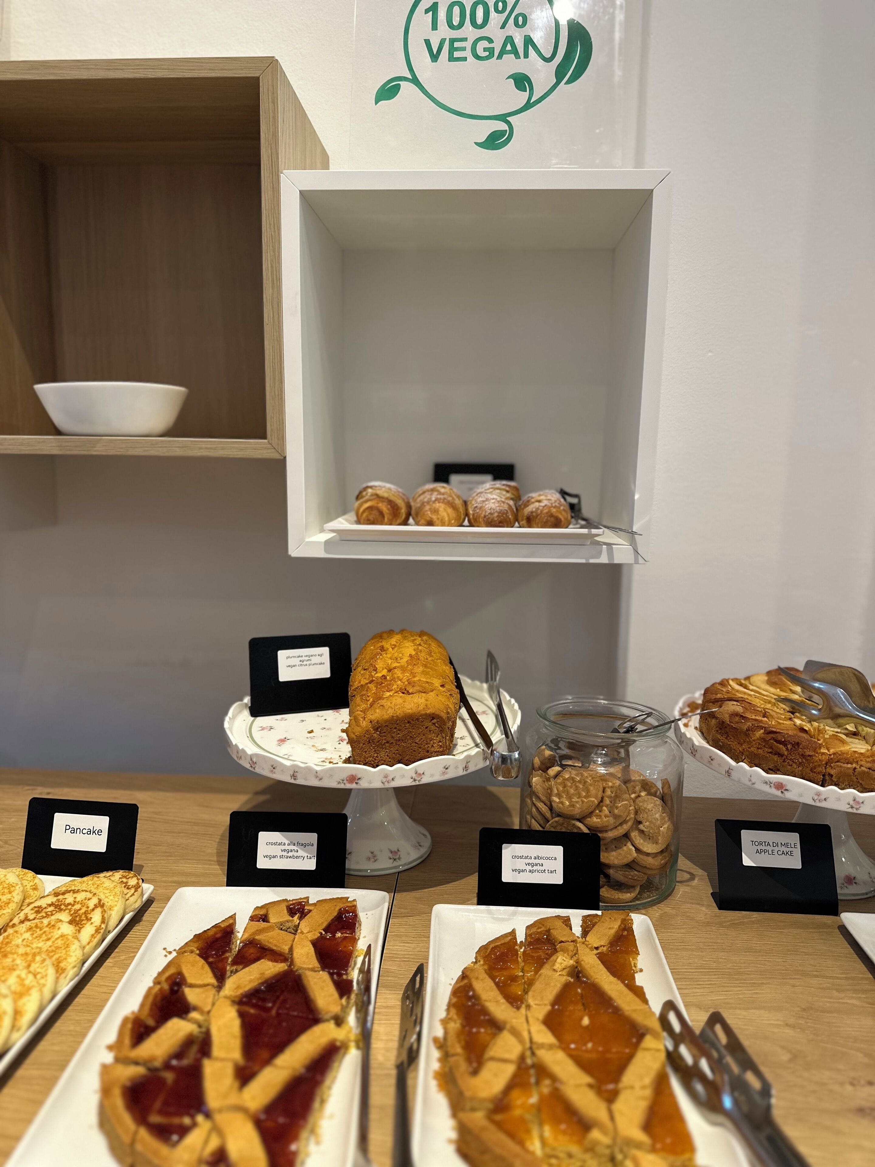 Une vitrine de boulangerie présentant divers produits de pâtisserie et desserts végétaliens, notamment une miche de pain, une tarte et un gâteau.