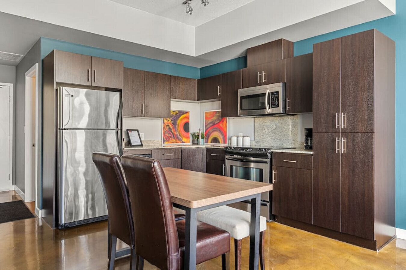 A modern kitchen with dark wood cabinets, stainless steel appliances, and a wooden dining table with leather chairs.