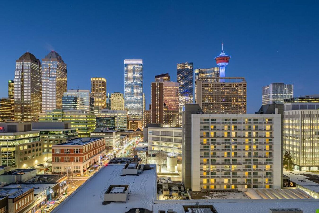 A cityscape with modern high-rise buildings, a prominent tower with a red and white spire, and a snow-covered rooftop.