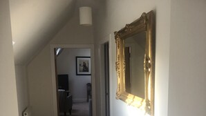 Un couloir doté d’un sol recouvert de moquette, d’un radiateur, d’un tableau encadré accroché au mur et d’un grand miroir décoratif.