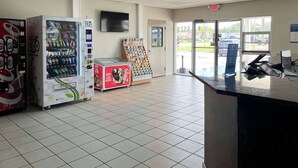 A clean, well-lit indoor space with vending machines, a display of snacks, and a counter with a computer. - Motel 6 New Port Richey, FL (New Port Richey)