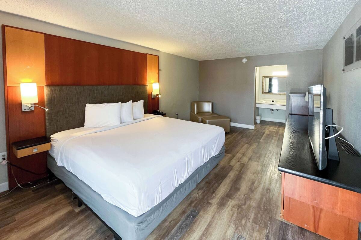 A hotel room with a large bed, a desk, a chair, a TV, and a bathroom visible through an open door.