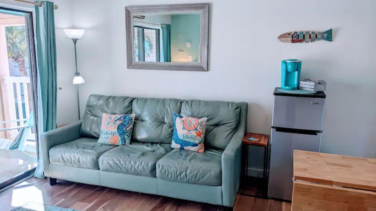 Een kamer met een groene leren bank, een klein bijzettafeltje, een koffieapparaat en een houten bankje.