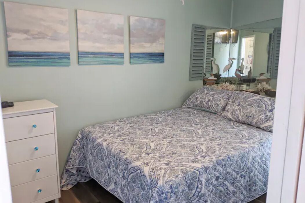 A bedroom with a bed, a dresser, and three wall paintings.