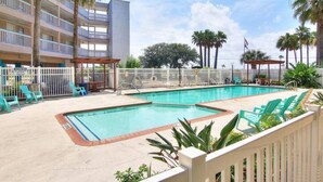 A hotel pool area with multiple levels of balconies, a fenced pool, and lounge chairs.