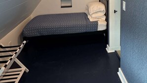 A small, dimly lit attic bedroom with a sloped ceiling, a single bed, a small table, and a chair. - Modern A-Frame | Walkable | Two Balconies | Views (Avalon)