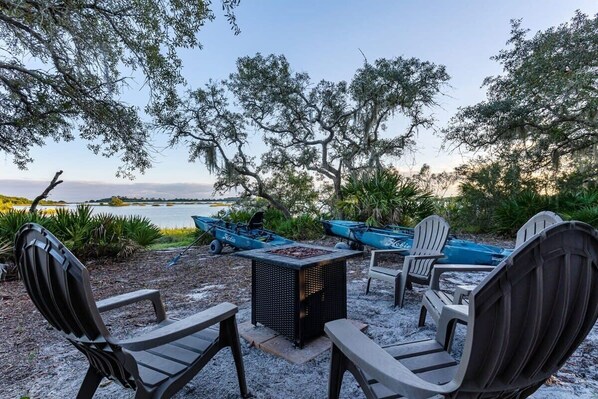 Outdoor seating with Adirondack chairs, a fire pit, and boats in the background.