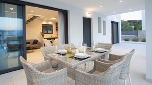 Un comedor moderno con una mesa de vidrio y sillas de mimbre, una cocina al fondo y vistas al exterior.