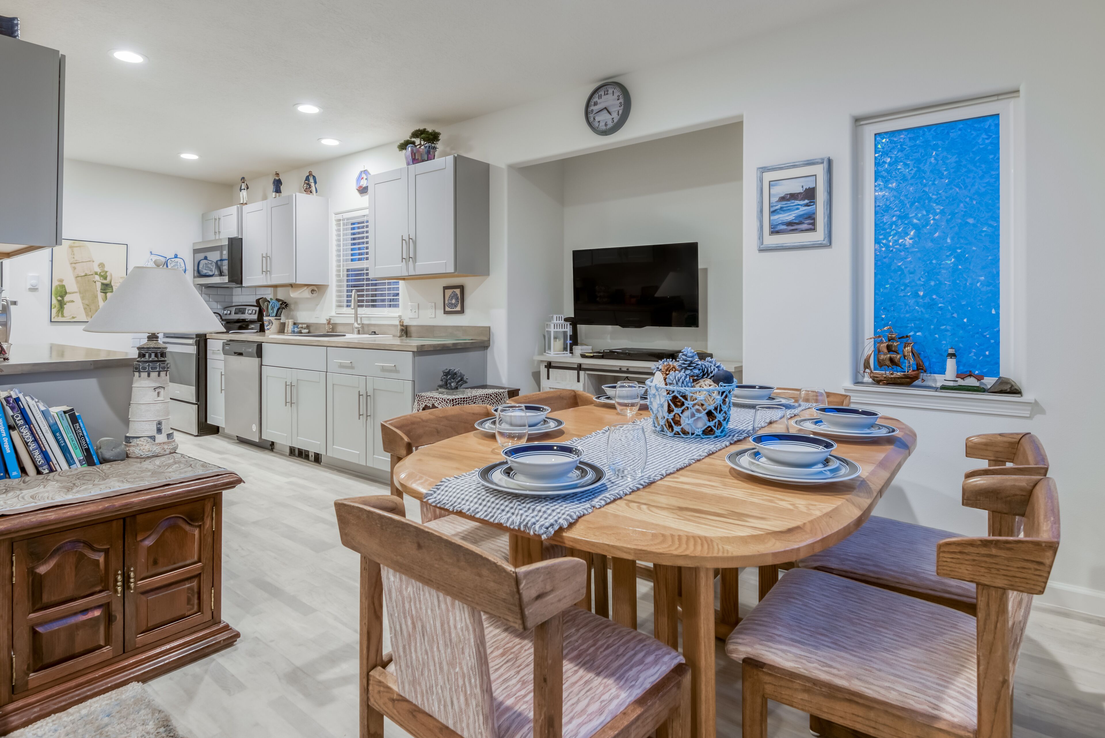 A modern kitchen with white cabinets, a dining table set with blue and white plates, and a large window with a blue view.
