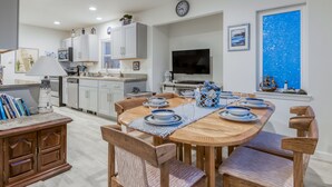A modern kitchen with white cabinets, a dining table set with blue and white plates, and a large window with a blue view. - Steps to the beach, ocean view, deck, BBQ, pet friendly with a fenced in yard (Lincoln City)