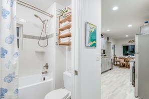 A modern bathroom with a bathtub, toilet, and shower. Adjacent is a kitchen with a dining area, featuring a map on the wall. - Steps to the beach, ocean view, deck, BBQ, pet friendly with a fenced in yard (Lincoln City)