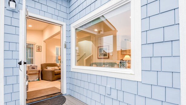 A modern home entrance with a wooden deck, a brown leather sofa, and a glass door leading to a living area with a staircase and a dining table. - Steps to the beach, ocean view, deck, BBQ, pet friendly with a fenced in yard (Lincoln City)