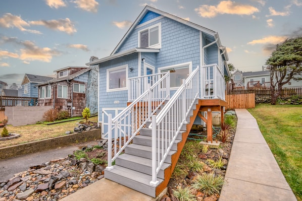 A two-story house with a blue exterior, white railings, and a wooden staircase leading to the front door.