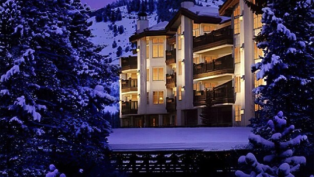 Un hôtel à plusieurs étages doté de balcons, entouré d’arbres couverts de neige et avec une chaîne de montagnes en toile de fond.