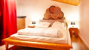Ein Schlafzimmer mit einem hölzernen Bett, einem roten Vorhang, zwei Nachttischen mit Lampen und einer Decke mit Holzbalken.