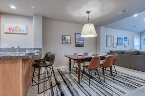 Une cuisine moderne dotée d’un comptoir en granit, de tabourets de bar et d’un coin repas avec une table et des chaises en bois.