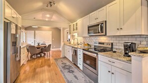 Una cocina moderna con armarios blancos, un refrigerador de acero inoxidable, un microondas y una estufa. Cuenta con un comedor con mesa y sillas.