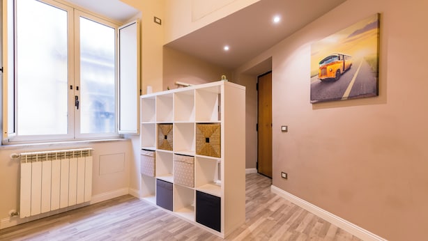 Un couloir avec un radiateur, une étagère blanche et un tableau représentant un autobus accroché au mur.
