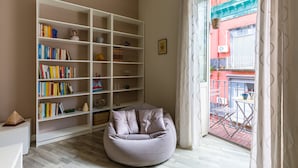 Un salon avec une grande bibliothèque blanche, un fauteuil rond en forme de poire et une vue sur un immeuble rouge, visible à travers une fenêtre.