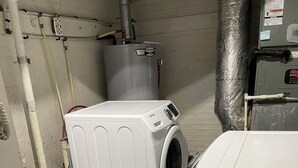 A laundry room with a front-loading washer and dryer, a water heater, and a utility room with a large water tank. - Private, Quiet Ap. “Morning Singing Birds”, close to Phoebe (Albany)