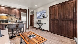 A modern kitchen with dark wooden cabinets, a stainless steel refrigerator, and a bar area with stools.