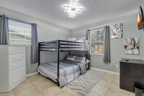 A bunk bed room with a dresser, a desk, and artwork on the walls.