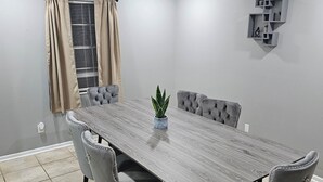 Ein Esszimmer mit einem langen Tisch, sechs Stühlen, einer Zimmerpflanze und einer Einbauschränken mit Dekoration.
