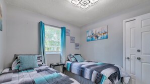 Ein Schlafzimmer mit zwei Betten, einem Fenster mit Vorhängen, einem Nachttisch und einer Tür.