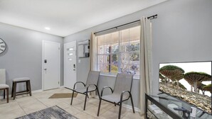 Ein modernes Wohnzimmer mit großem Fernseher, einer Sitzecke und Blick auf Bäume durch das Fenster.