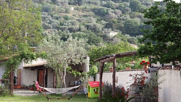 Een tuin met een hangmat, een klein speelhuisje en een houten pergola.