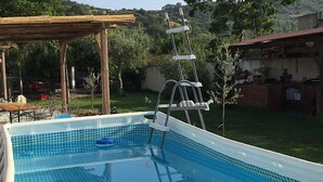 Een buitenzwembad met een houten pergola, een zwemtrap en een bakstenen muur op de achtergrond.