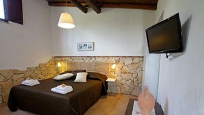 Een slaapkamer met een stenen muur, een bed met donkere dekbedovertrek, een wandtelevisie en een stenen openhaard.