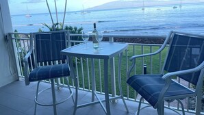 Ein Balkon mit zwei Stühlen und einem Tisch, der Blick auf einen Strand mit Booten und Palmen bietet.