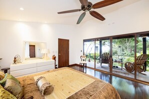 Un dormitorio amplio con una cama grande, un ventilador de techo y una puerta corrediza de vidrio que da a un balcón con mobiliario exterior.