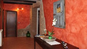 A room with a red wall, a wooden door, a small table with a vase of flowers, and a hanging picture frame.