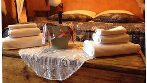 A neatly arranged room with a bed, pillows, towels, a glass of wine, and a basket with a pink ribbon.
