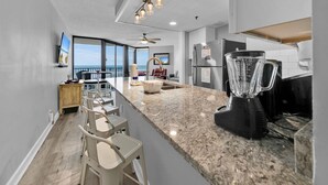 Cocina moderna con encimera de granito, una licuadora, un refrigerador y una zona de comedor con taburetes de bar.