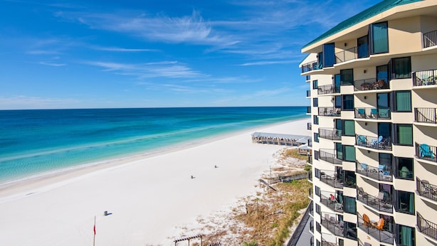 Un hotel frente a la playa con balcones, una playa y cielos despejados.