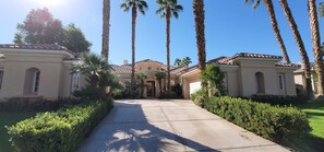 A large, two-story building with a symmetrical facade, a central entrance, and a well-maintained garden with palm trees and hedges.