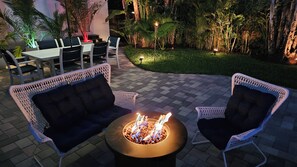 An outdoor seating area with wicker chairs and a central fire feature. - Capri Cottage, Pool, walk to restaurants! (West Palm Beach)
